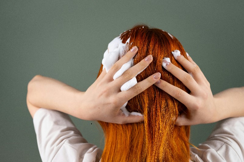 Person mit roten Haaren massiert weißen Schaum ins Haar.