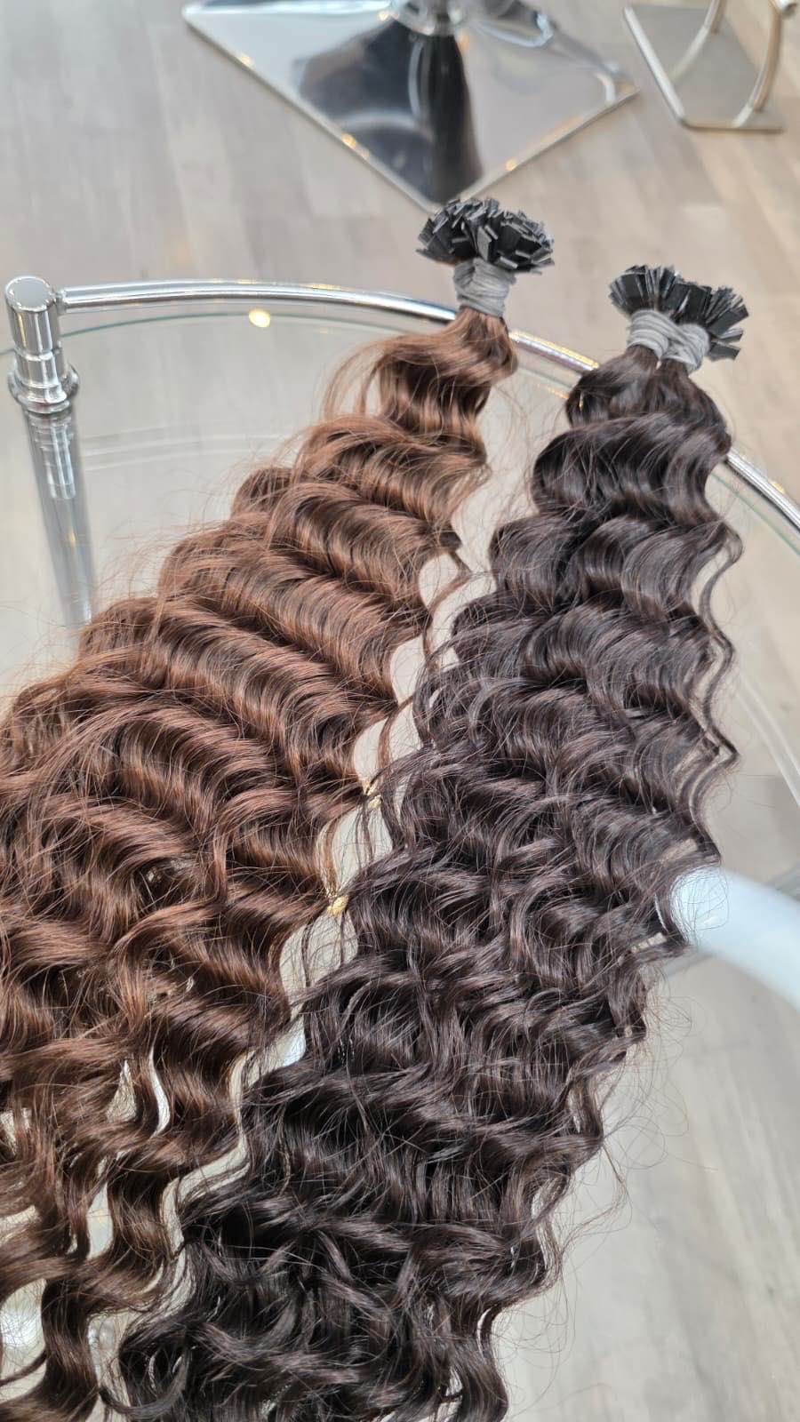 Zwei Bündel lockiger Haarverlängerungen in Braun und Schwarz, bereit zur Einarbeitung im Friseursalon.