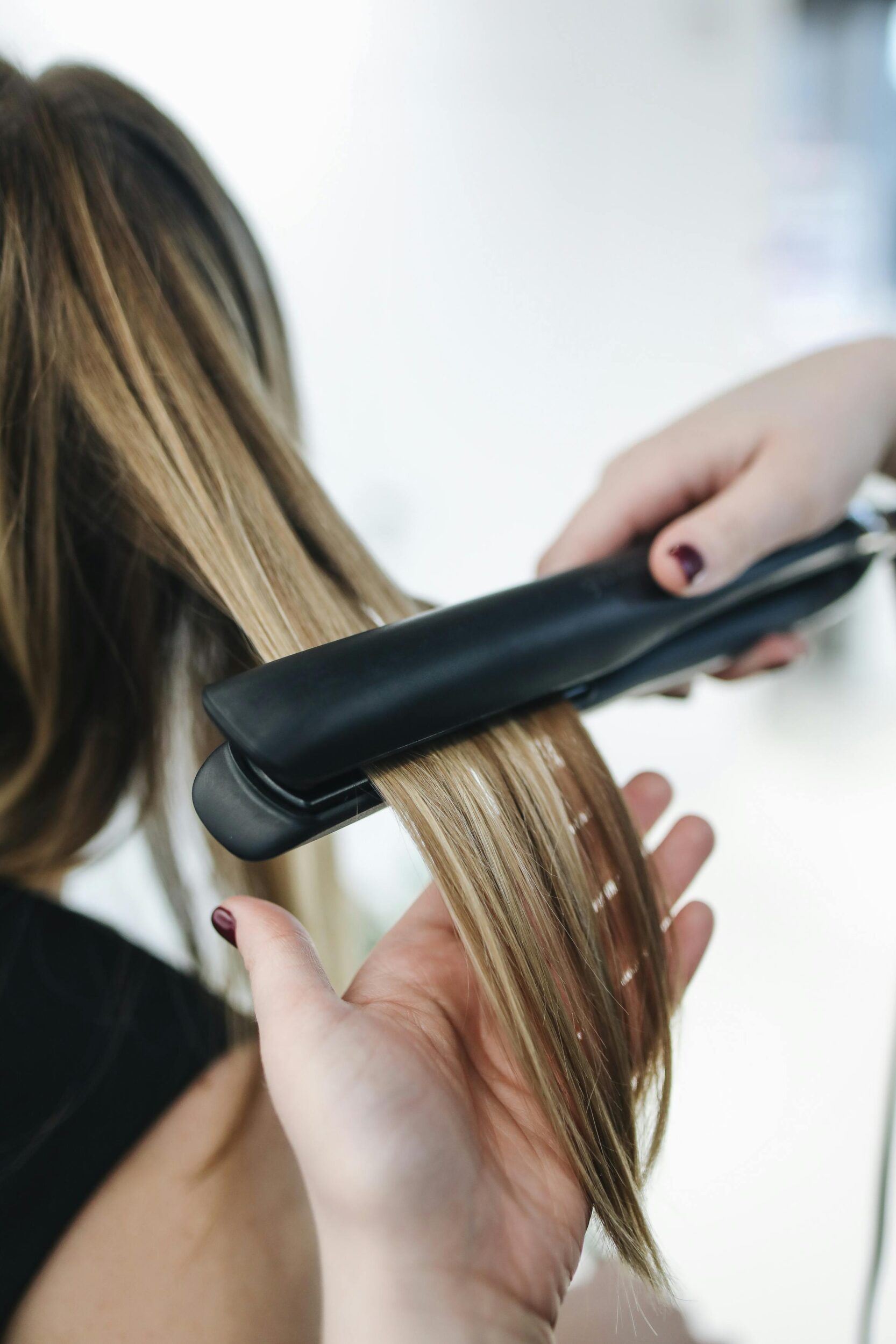 Friseurin glättet lange blonde Haare mit einem Glätteisen im Salon.