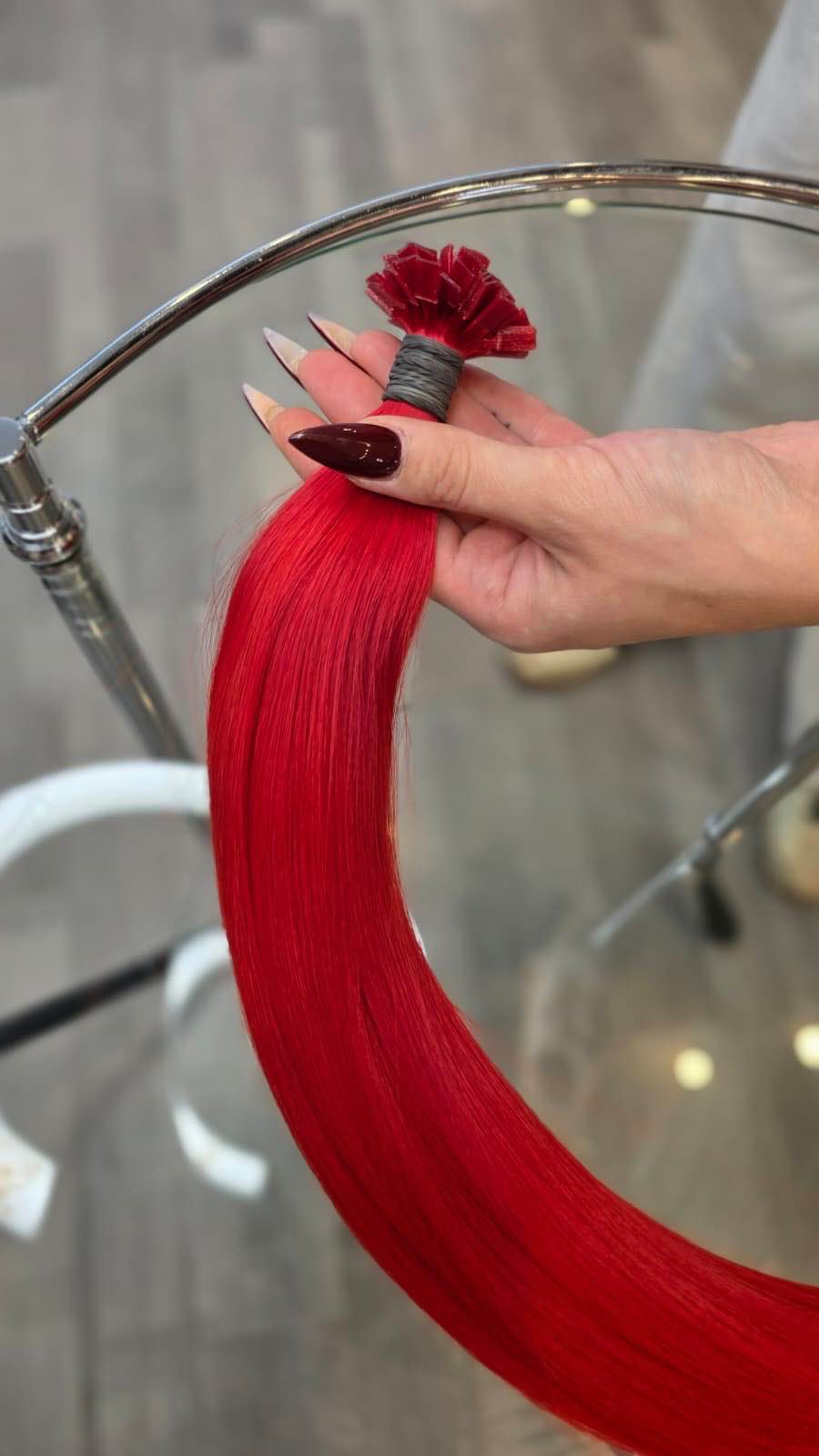 Hand hält ein Bündel glatter, roter Echthaar-Extensions zur Haarverlängerung im Friseursalon.