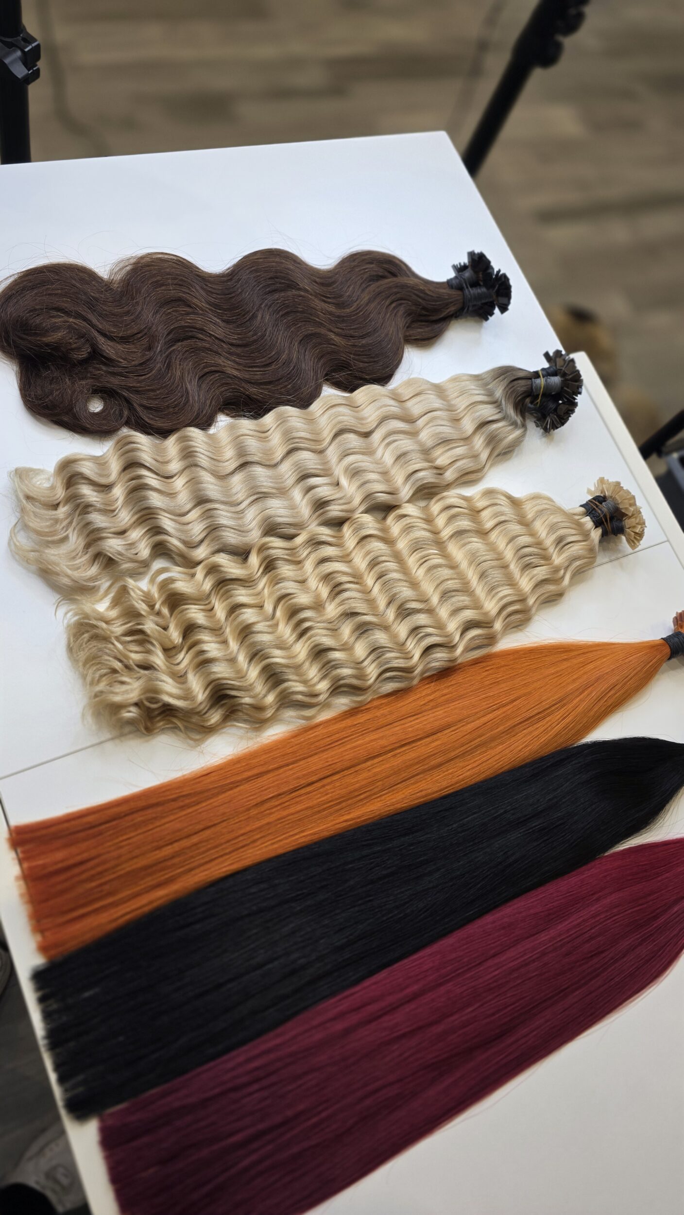 Extensions-Strähnen in verschiedenen Farben und Dicken liegen ordentlich nebeneinander auf einem Friseurtisch.