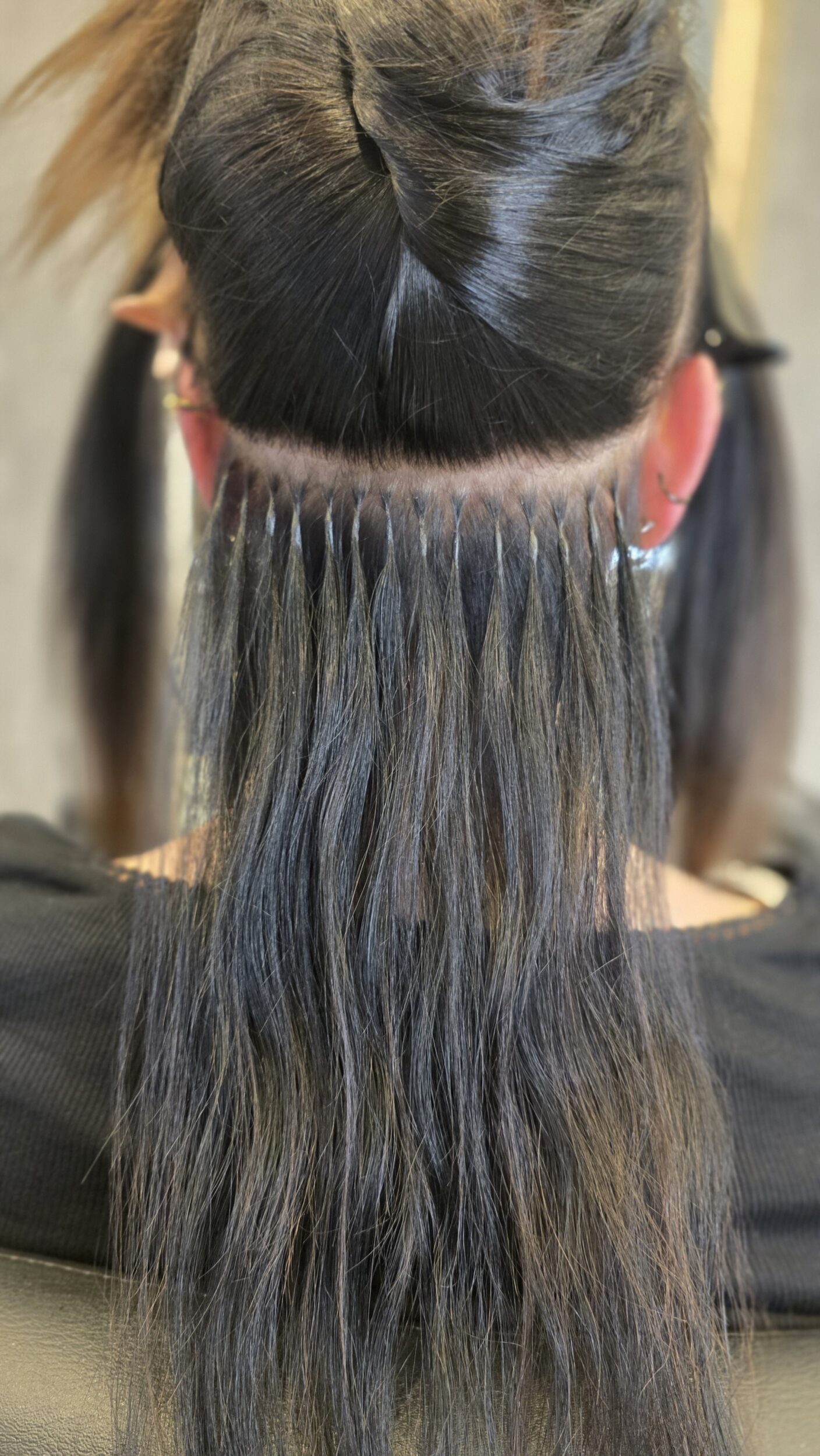 Friseurin setzt Bonding- oder Tape-Extensions in feines Haar ein – Nahaufnahme der Hände.